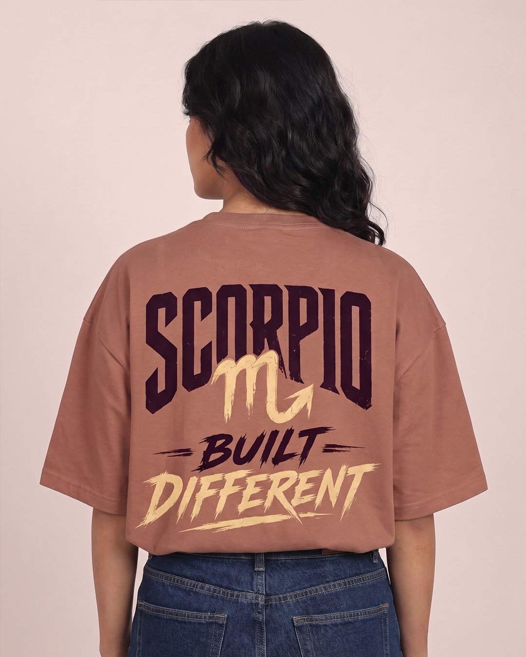 Scorpio Built Different Printed Brown T-shirt Woman wearing RHINO RAVE brown oversized T-shirt with “SCORPIO – BUILT DIFFERENT” graphic print on the back, paired with blue jeans.