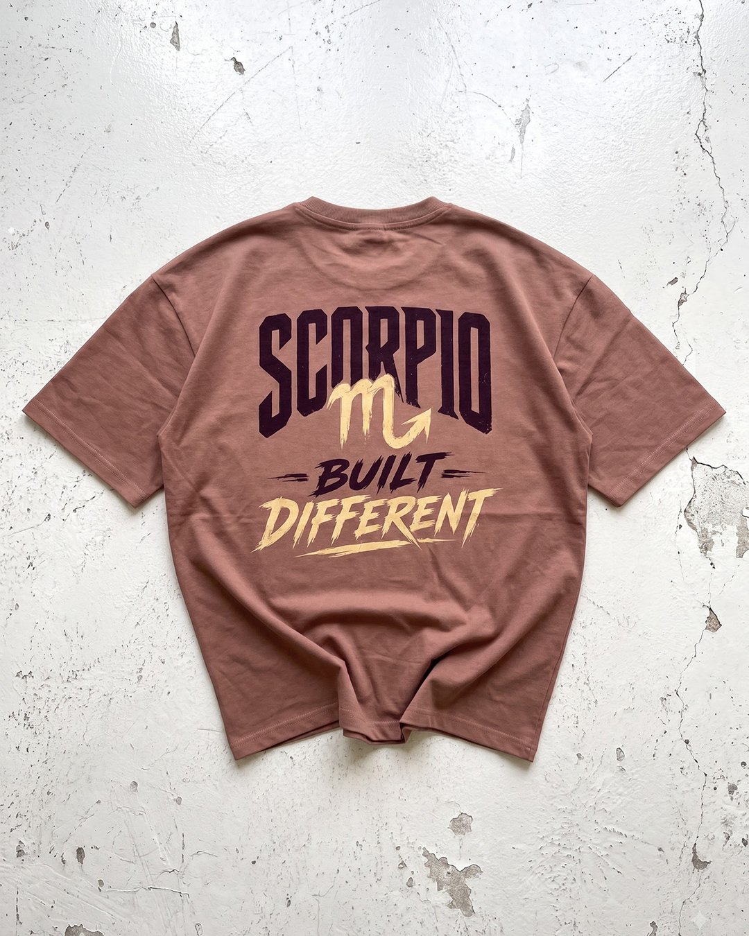Rhino Rave Brown T-shirt laid flat on a textured white surface, featuring a large “SCORPIO – BUILT DIFFERENT” graphic on the back.